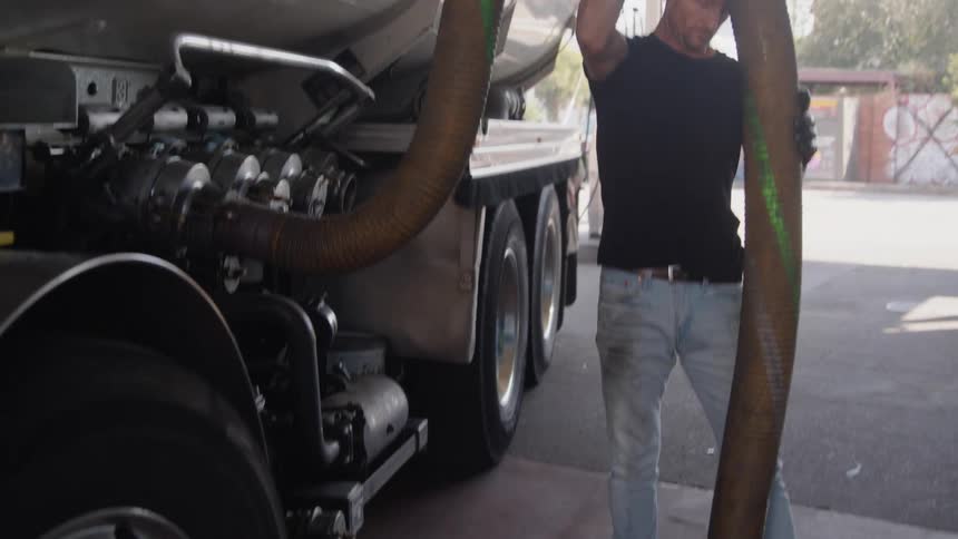 A man attaches the hose from the truck at the gas station