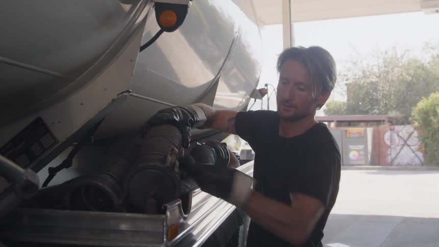 A man loads a hose onto a tray on the outside of a truck during the day