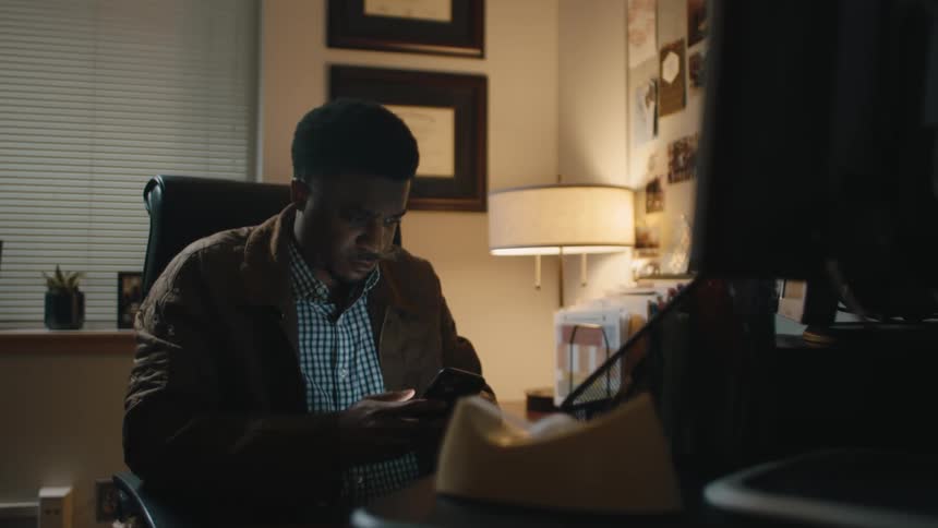 A man is sitting indoors and texting on a cell phone