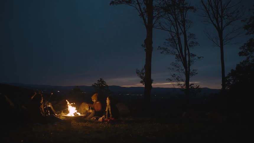 A small group of people sitting around a campfire with their dog