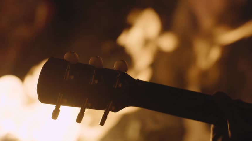 A musician plays guitar near a campfire at night
