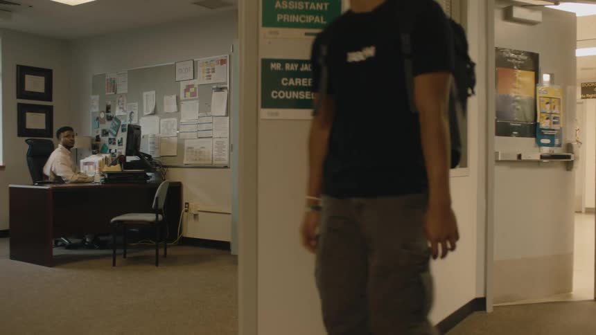 A boy opens a door and walks past the assistant principals office looking bored and half asleep