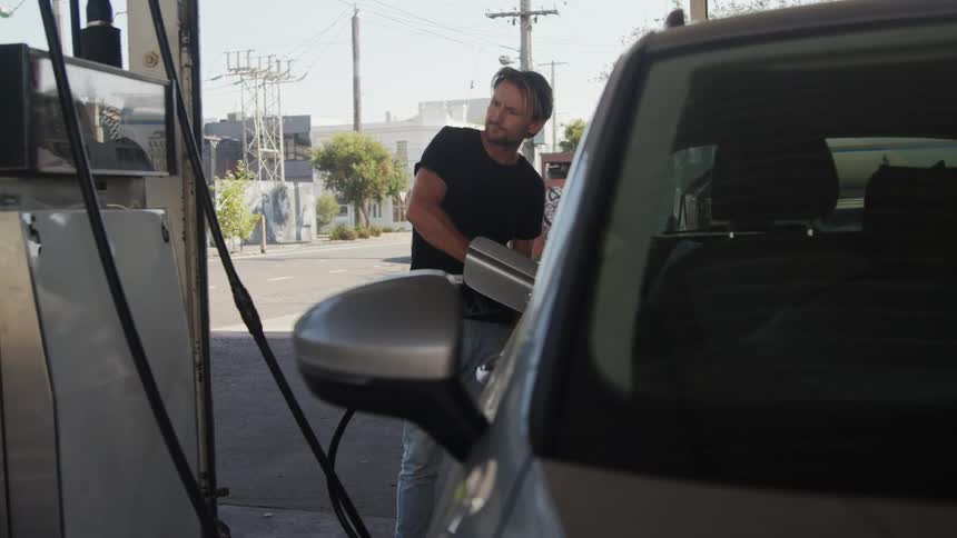 A man is standing next to an automobile as he fills it with gas
