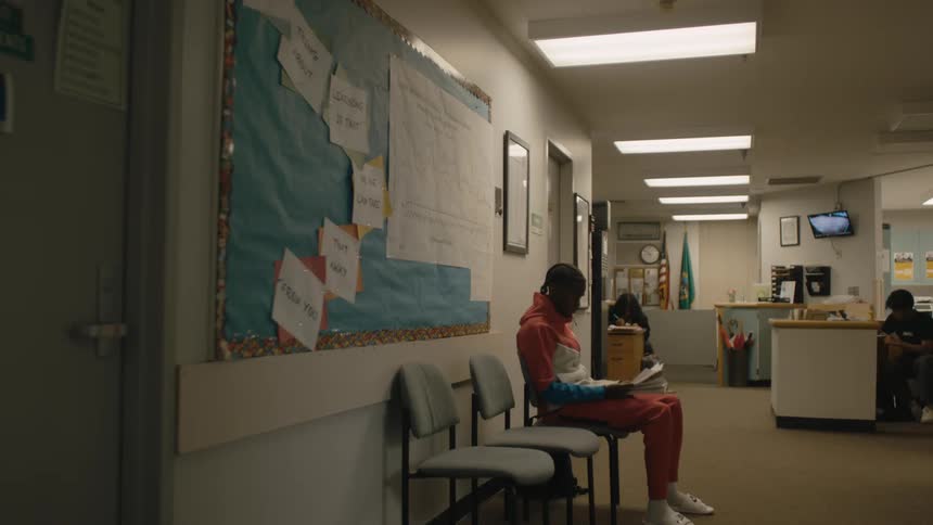 A boy sitting reading outside a counselors office in a high school