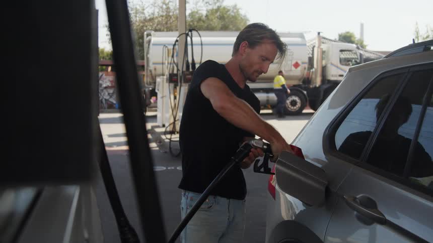 A man puts a gas pump into an automobile as he fills it with gas and puts it back on the pump and screws on his gas cap