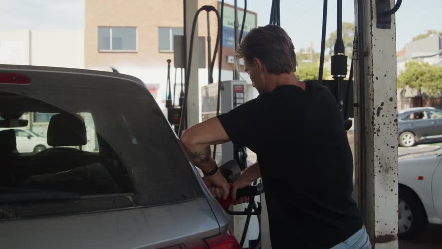 Bored man in a black shirt pumping gas at a gas station