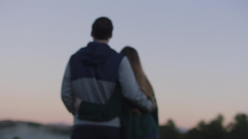 A couple standing with their arms around each other looking out at the fog over tree tops