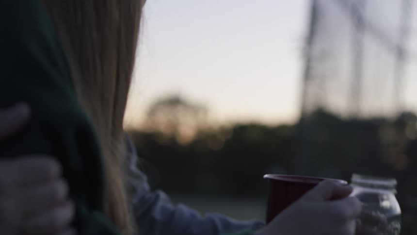 A man fills his girlfriend's coffee mug from a jar as they sit outside