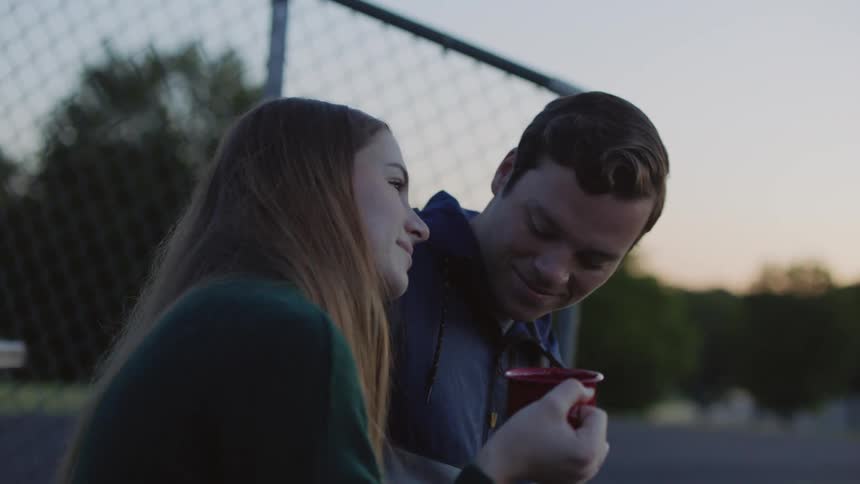 A young man puts his arm around a young woman outside