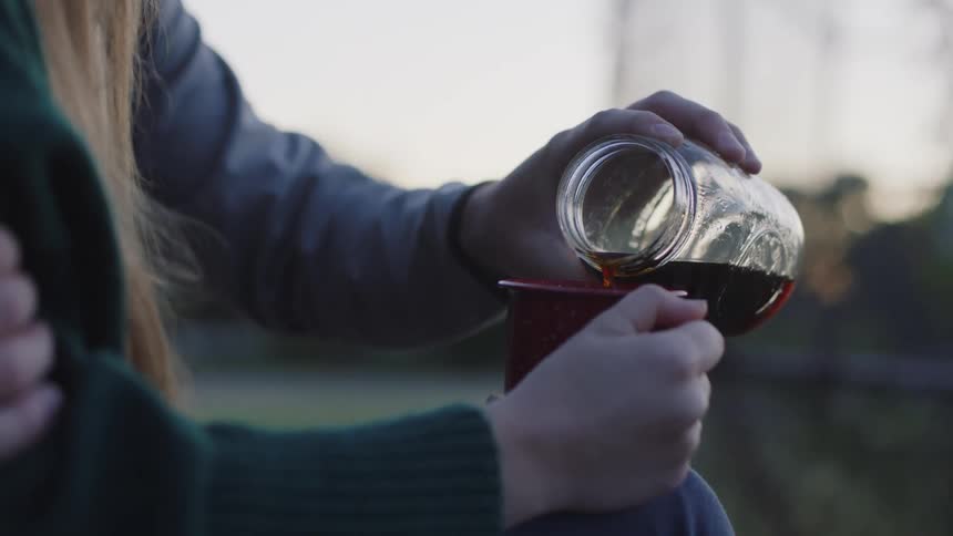 A man pours his cup of coffee into a woman's coffee cup outside