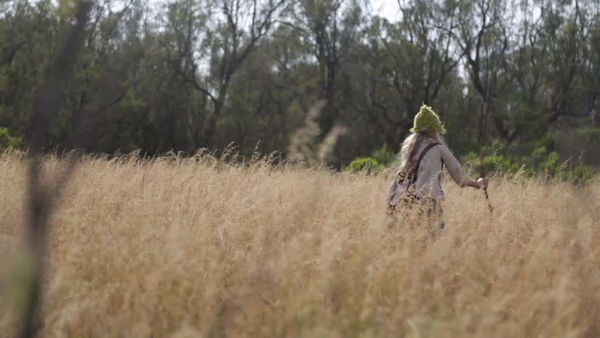 A girl walks in the grass with a stick