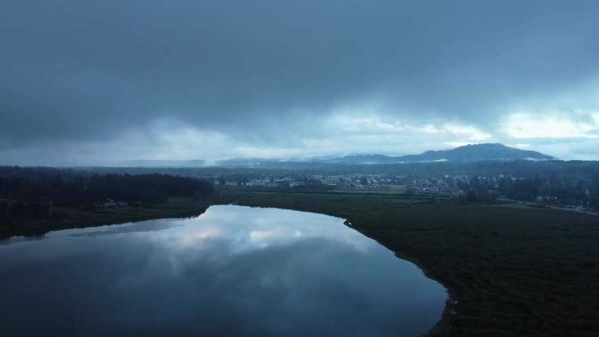 Sky reflects from glass like surface of lake sitting near town and forest