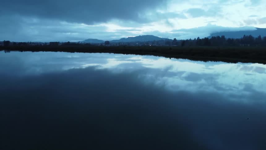 The smooth surface of the lake reflects the sky and dark clouds above
