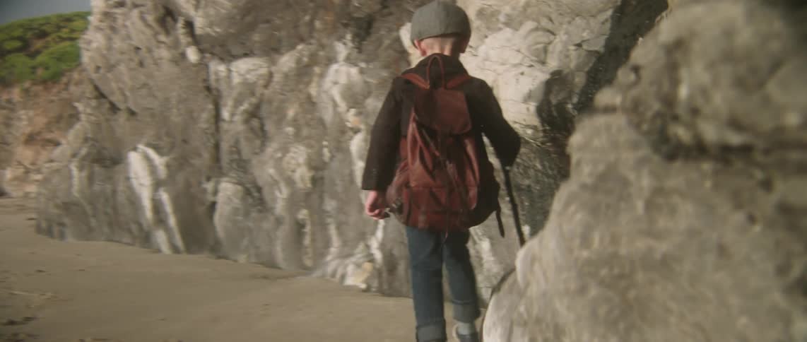 A boy is walking along some rocks on a cloudy day