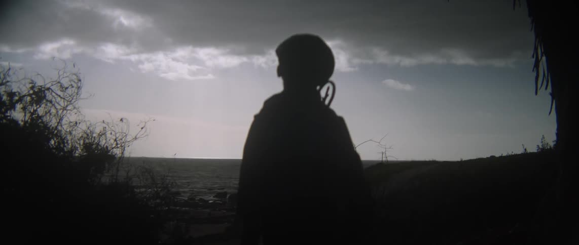 A child is standing in a dark area with some heavy clouds by the water