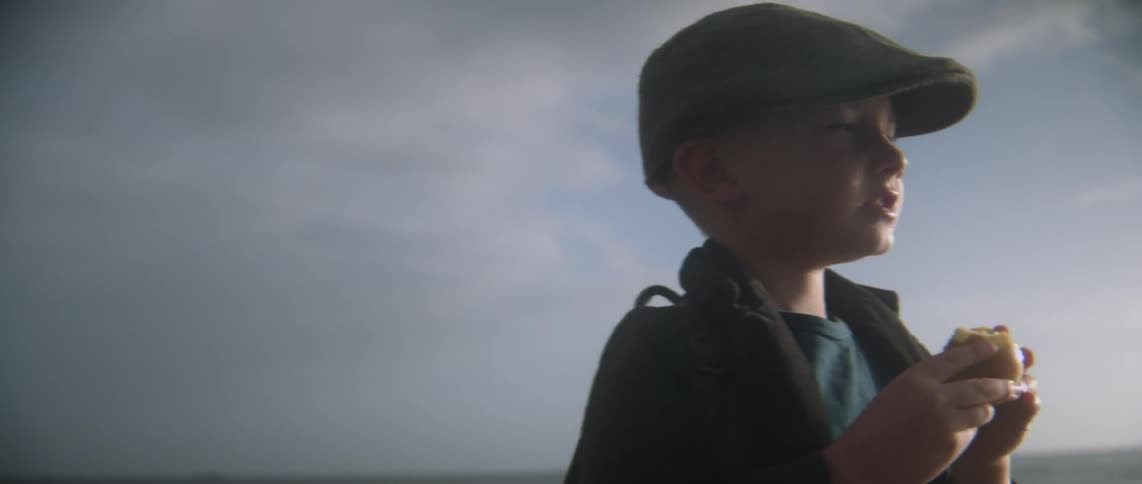 A boy wearing a hat is eating outdoors