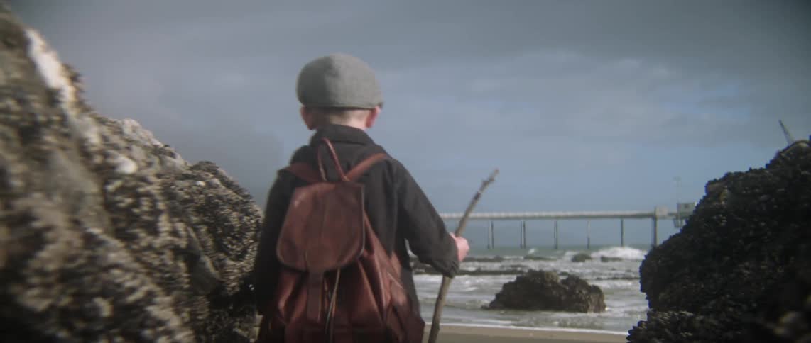 A boy walks between some rocks towards the water