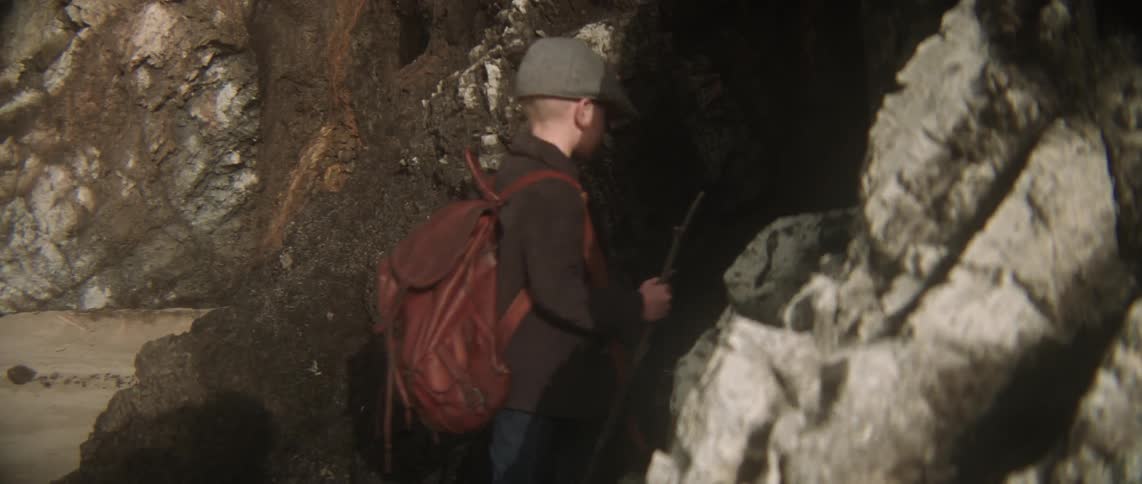 A young boy with a walking stick approaches a cave