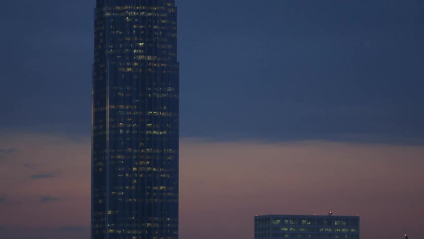 A very tall building is lit in this city at dawn