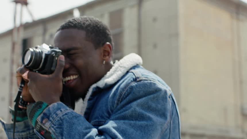 A man smiles while taking photos with a camera outdoors