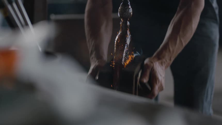 A craftsman uses two heat resistant pads to shape hot glass
