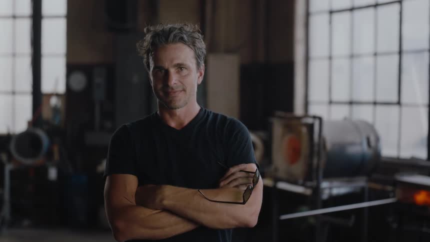 A man poses with his arms crossed while standing in his studio
