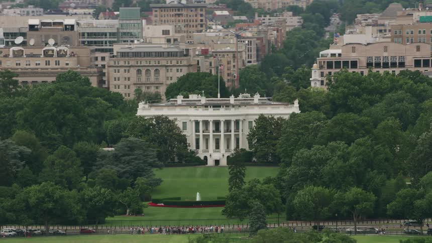 The american flag flies above the white house with tourists gathered at the gate