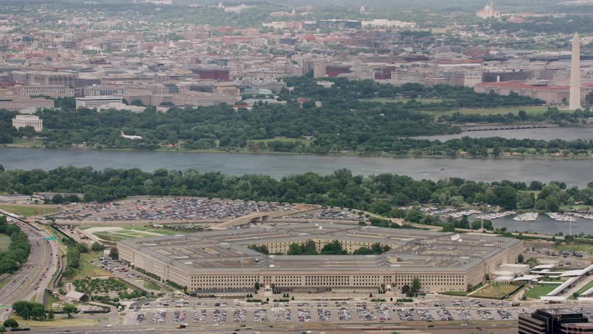 An airplane flies over the pentagon preparing to land with the washington monument and city behind