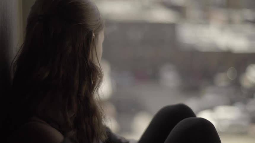 A woman is sitting near a window looking out