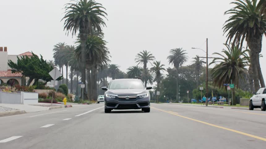 A car travels down the road through a residential area on a cloudy day