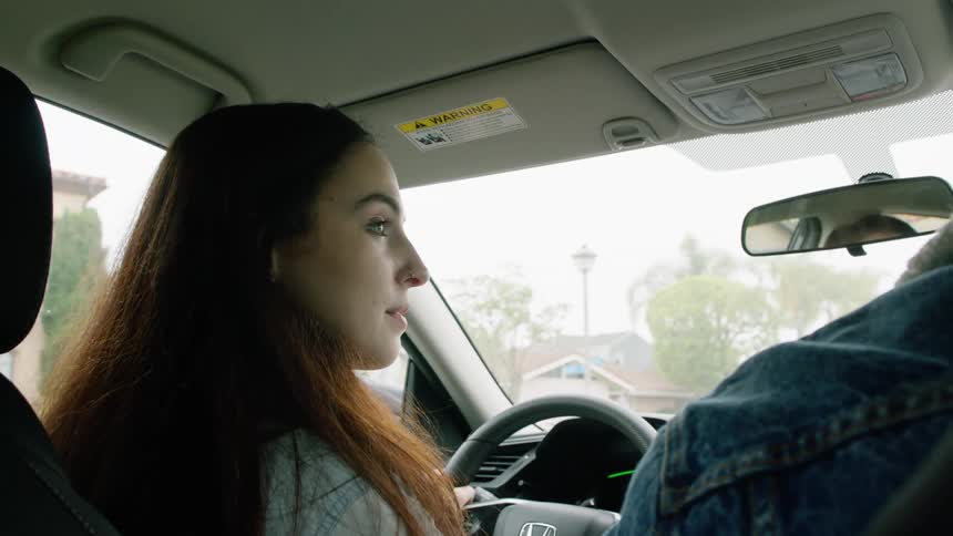 A young woman smiles while driving a car through a neighborhood