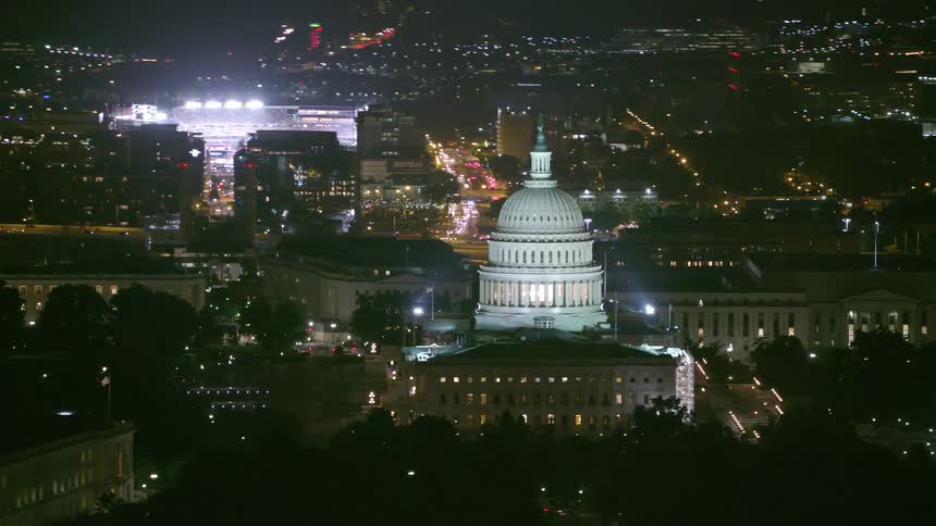 The dome of the united states capitol building and the city is lit up at night