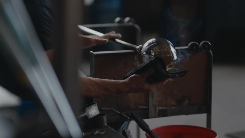 Male glass maker rotates glass and uses cloth to shape it