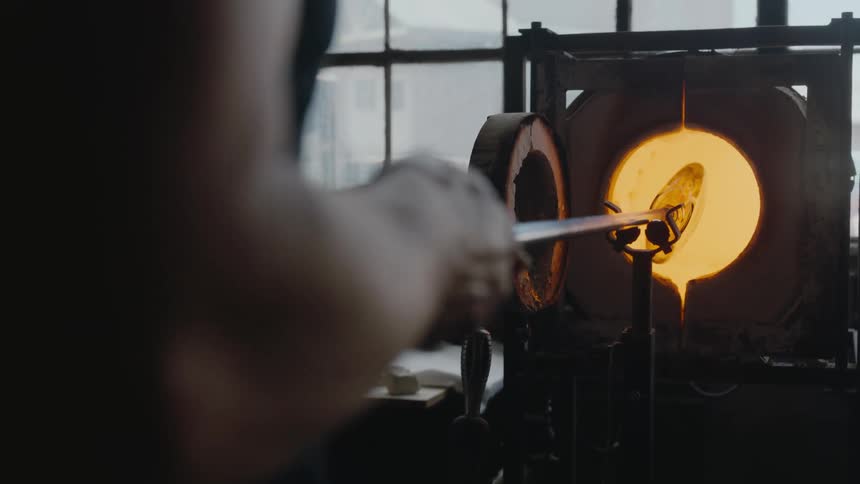 A glassmaker spinning glass inside of kiln