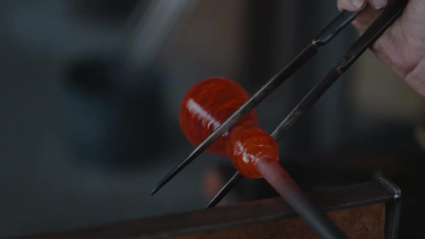 A man uses tools as he shapes glass