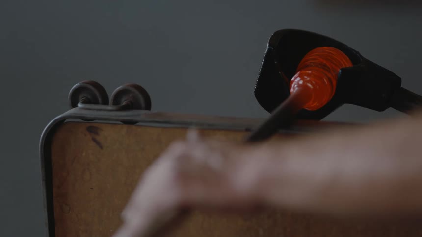 An artist rolling glass to cool it off with specialty tools