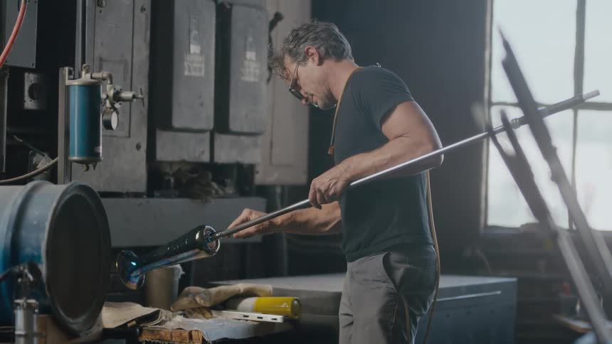 A glass maker spinning a new piece of art with backlight