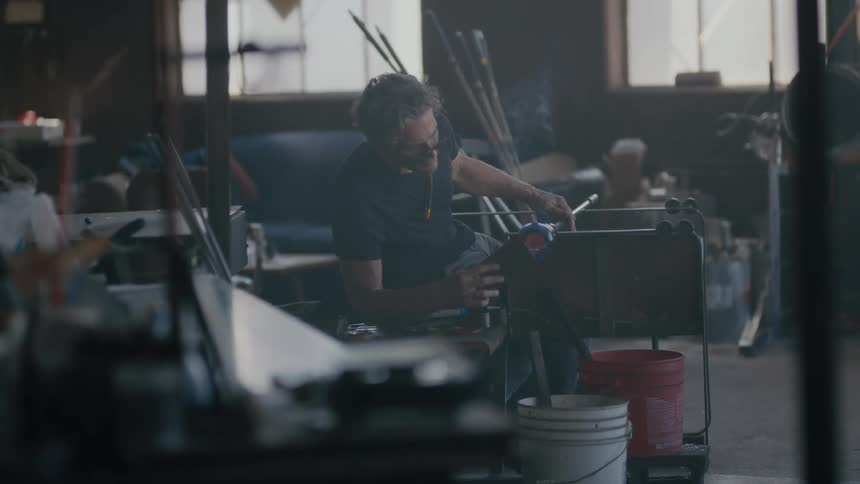 A backlit glass maker looking cool works on a new piece of art