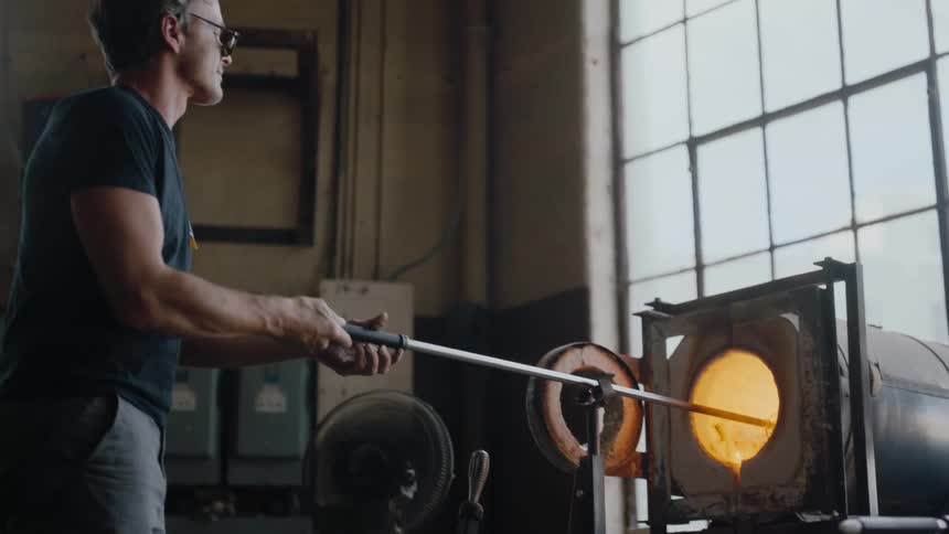A glass maker spins a new piece in furnace