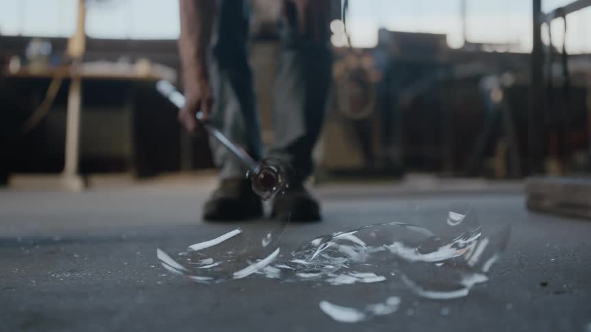 A glass maker smashes a sphere of clear glass on the floor of his studio