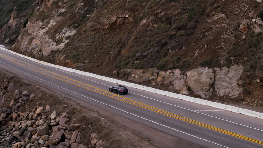 Cars are traveling on a coastal mountain highway on an overcast day