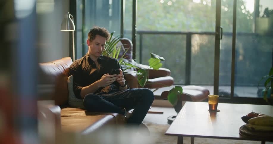 Man sits in living room smiling as he scrolls on smartphone
