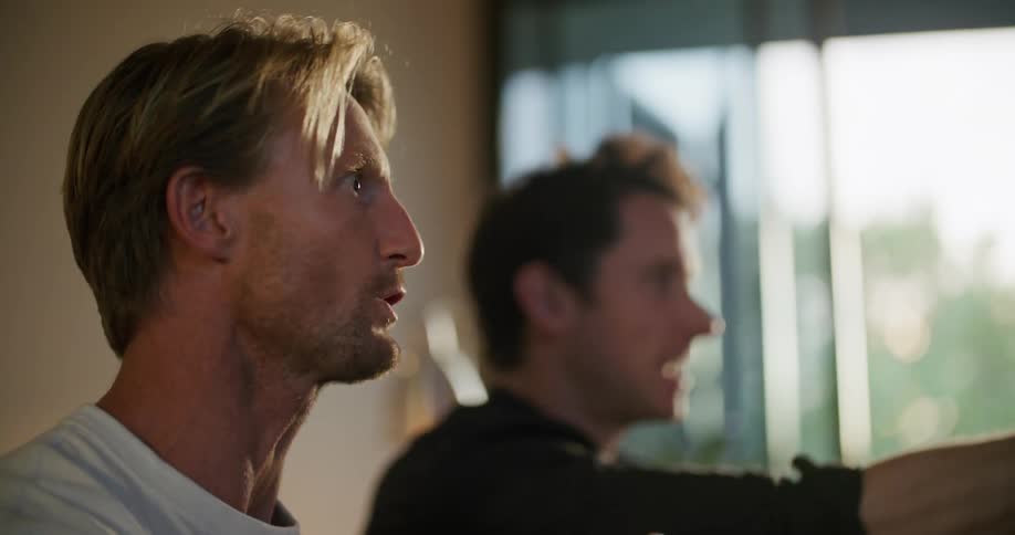 Two men leaning forward cheering and fist pumping while watching sports