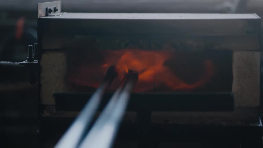 Poles reach inside a kiln as flames burn in artisan studio