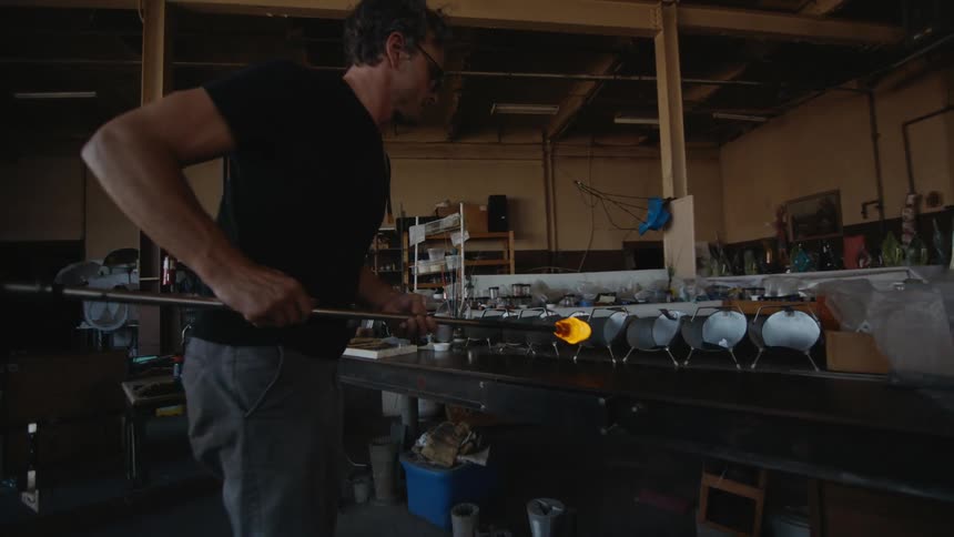 An artisan glass blower man spins glass in his gritty workspace