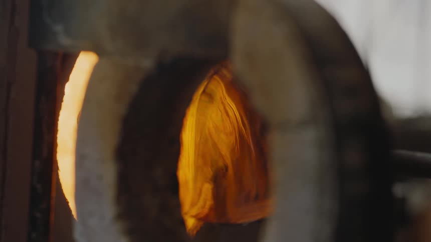 Glass blower spinning glass in hot oven