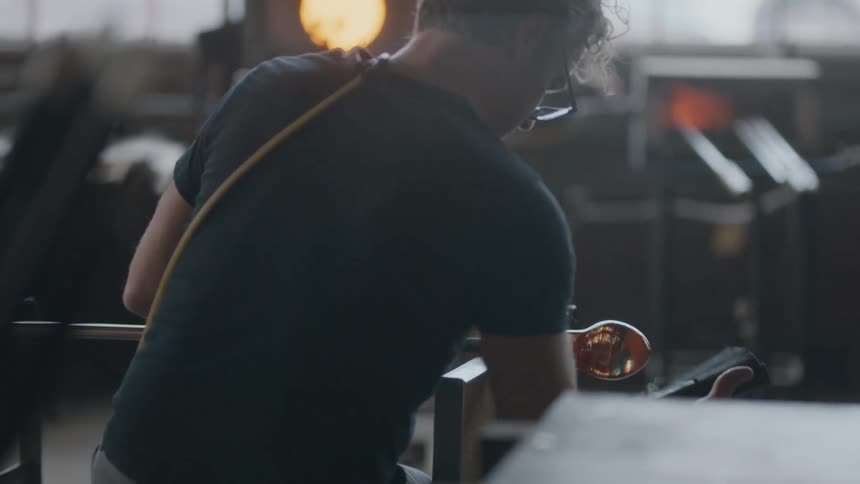 A glass blower shaping a new work of art in his studio with kiln burning