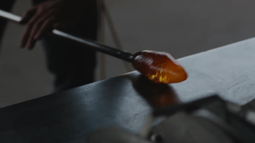 Rolling hot glass in glass blower artisan studio