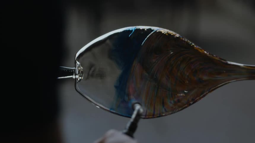 Glass blower firing and spinning a vase with beautiful colors