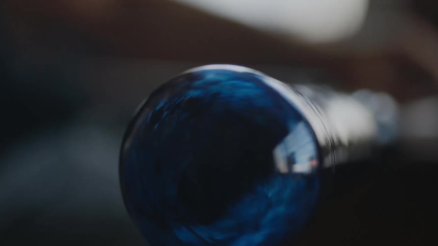 Close up of spinning blue glass as the artist cools off his work of art